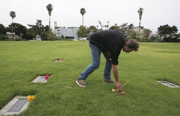 
Rod Kirby makes his daily rounds placing flowers on the tombstones at Cemetary Memorial Park on Wednesday in Ventura. Two signs have been posted at the ceremony honoring the 3,000 people buried there. 